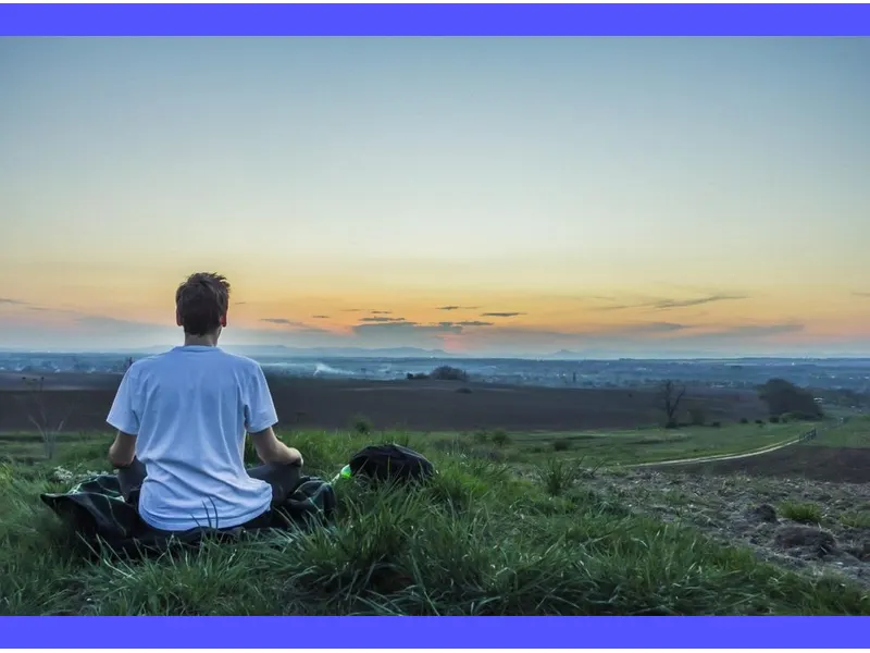 Persona in meditazione, immersa in un paesaggio tranquillo e sereno, mentre cerca la serenità interiore attraverso la preghiera e la contemplazione.